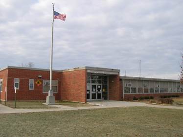 A school building with a flag pole

AI-generated content may be incorrect.